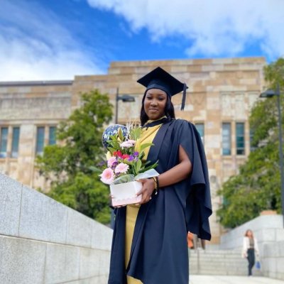 A young African woman stands in graduation cap and gown and holding flowers outside 澳门七星图's sandstone Great Court.